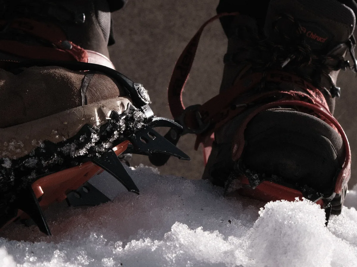Close-up of hiking boots fitted with metal crampons on snowy ground