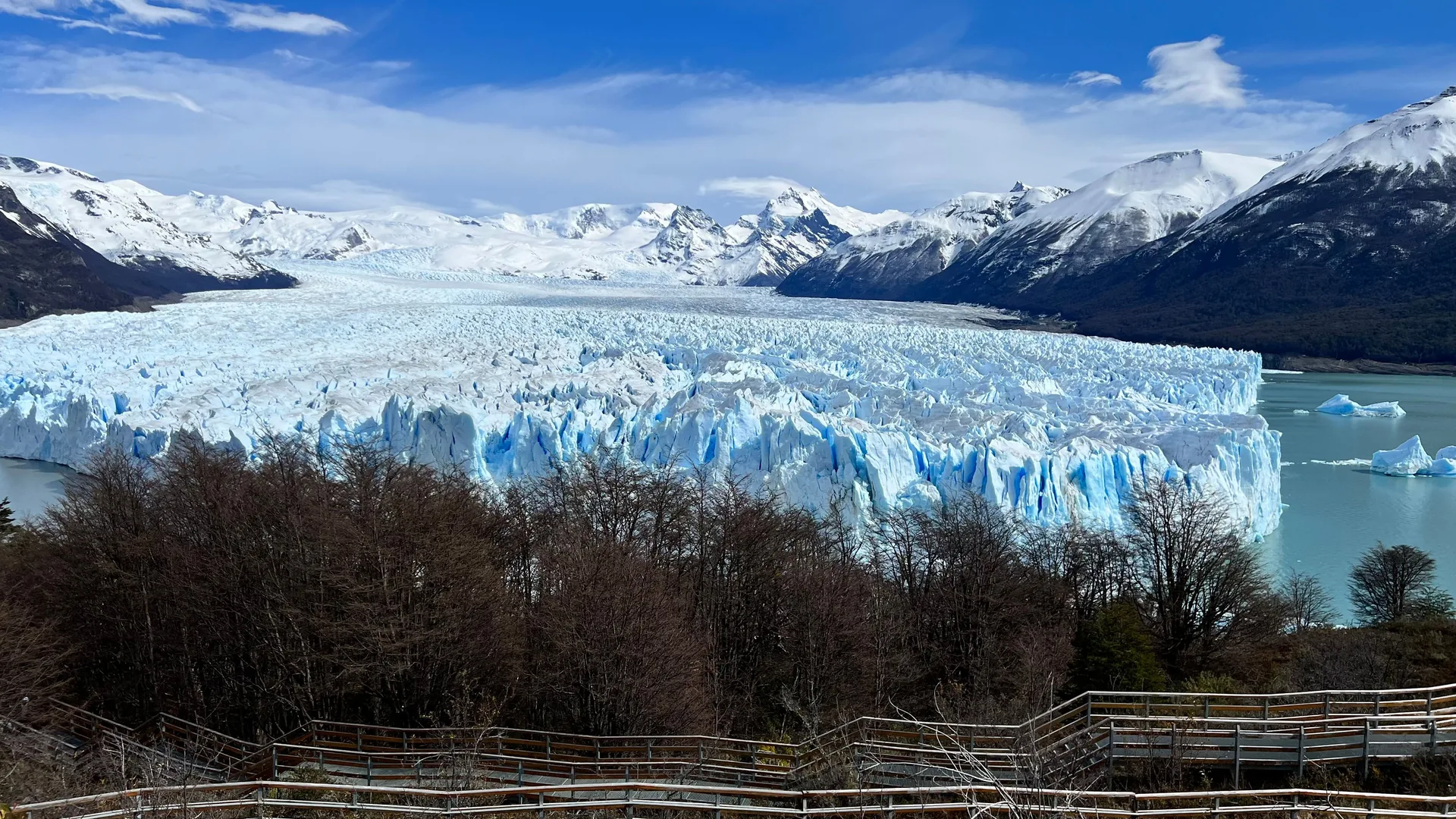Wide view of Perito Moreno Glacier's jagged blue-white ice front above the lake, with snow-capped peaks behind